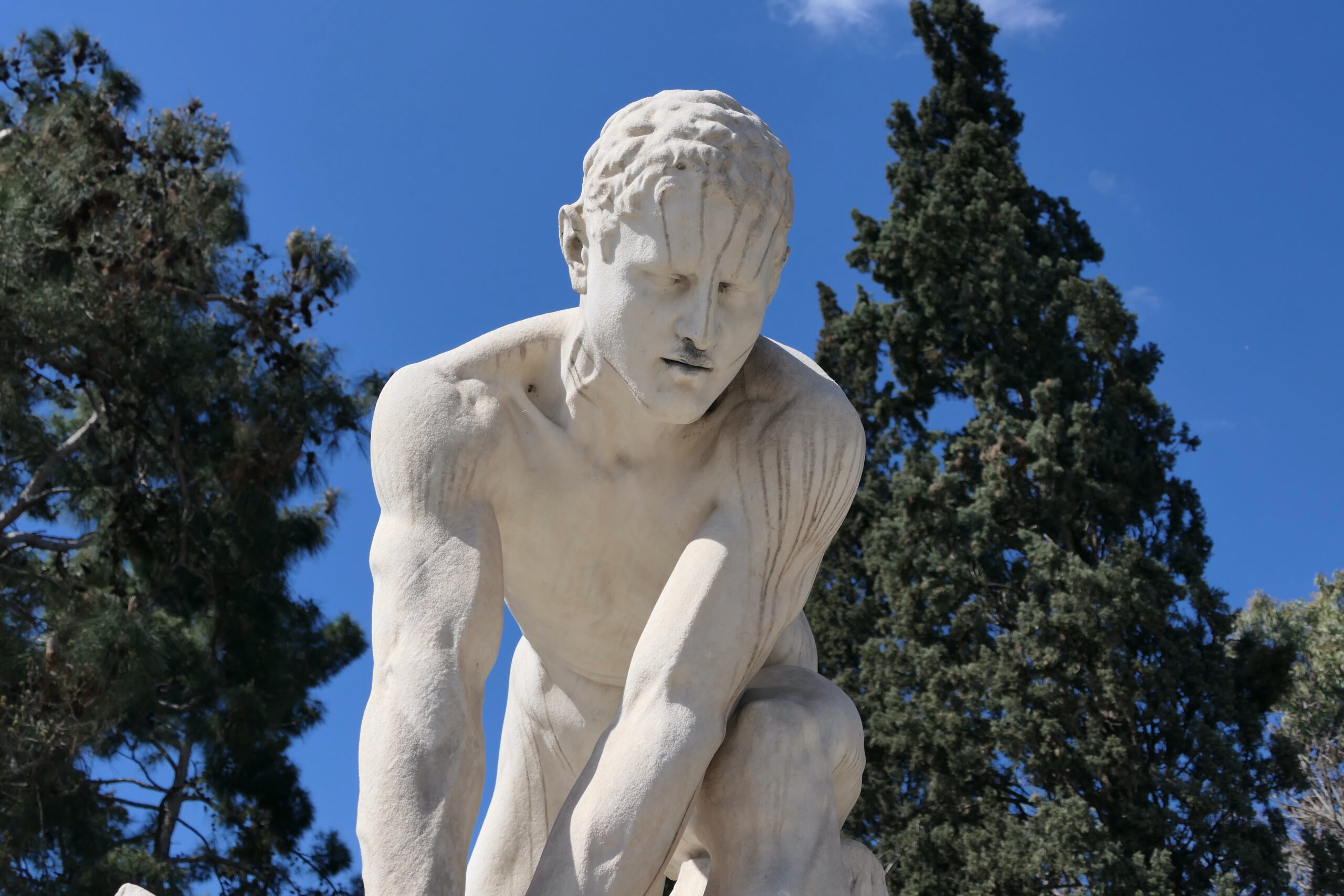 Mitten in Athen steht der in Marmor gehauene Mann, der seit Jahrhunderten versucht, einen Ast abzubrechen mit schmerzverzerrter Miene.