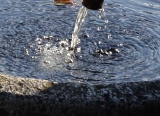 Eiskalt rinnt das Wasser aus der eisernen Röhre ins ovale Granitbecken des Brunnens.