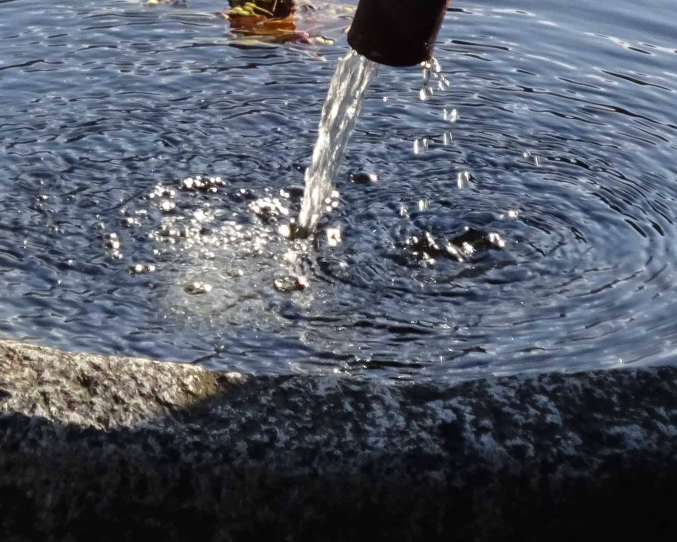 Eiskalt rinnt das Wasser aus der eisernen Röhre ins ovale Granitbecken des Brunnens.